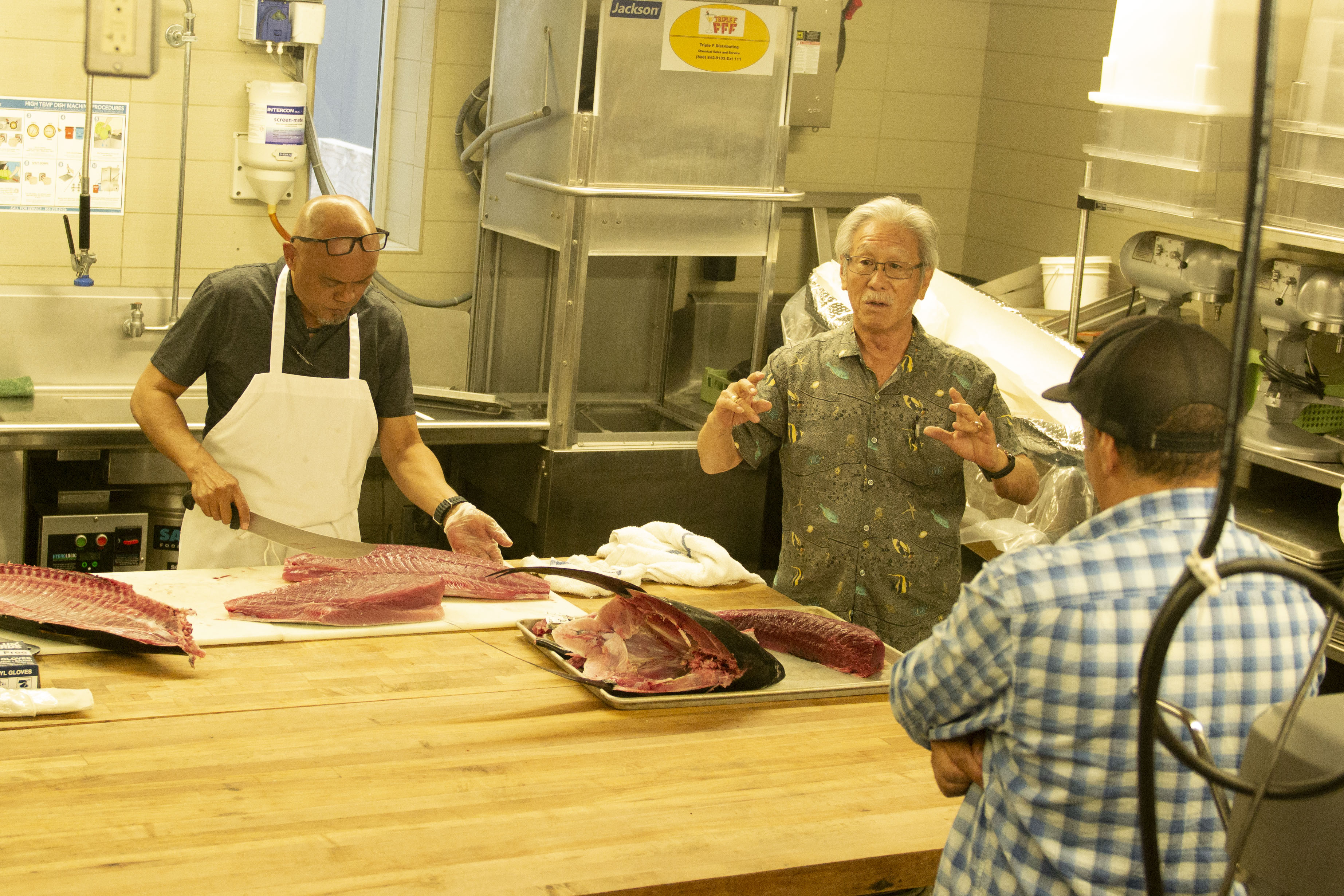 Brooks Takenaka, the general manager of the United Fishing Agency, (right) speaks to workshop attendees as Nelson Aberilla breaks down an ahi at the Hawai‘i Community College – Palamanui campus Kona. 