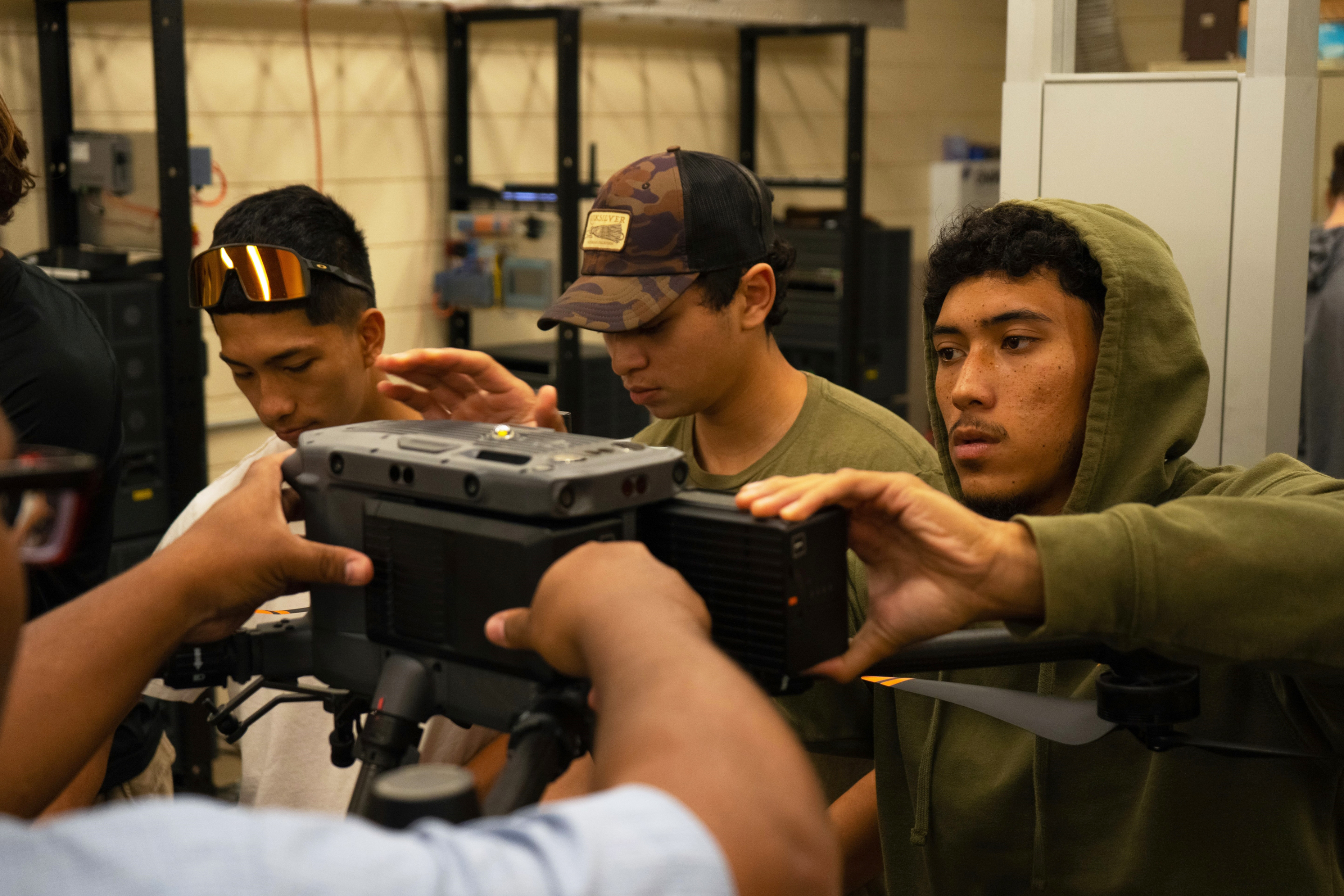 (L-R) Isaac Mandaloniz, Thomas Costa and Khayden Kahihikolo insert batteries in the DJI Matrice 350 RTK drone to prepare it for flight. ENGT 107 equips students with a comprehensive introduction to drone operations, including preparation for the FAA Part 107 certification required to become a licensed commercial drone pilot.